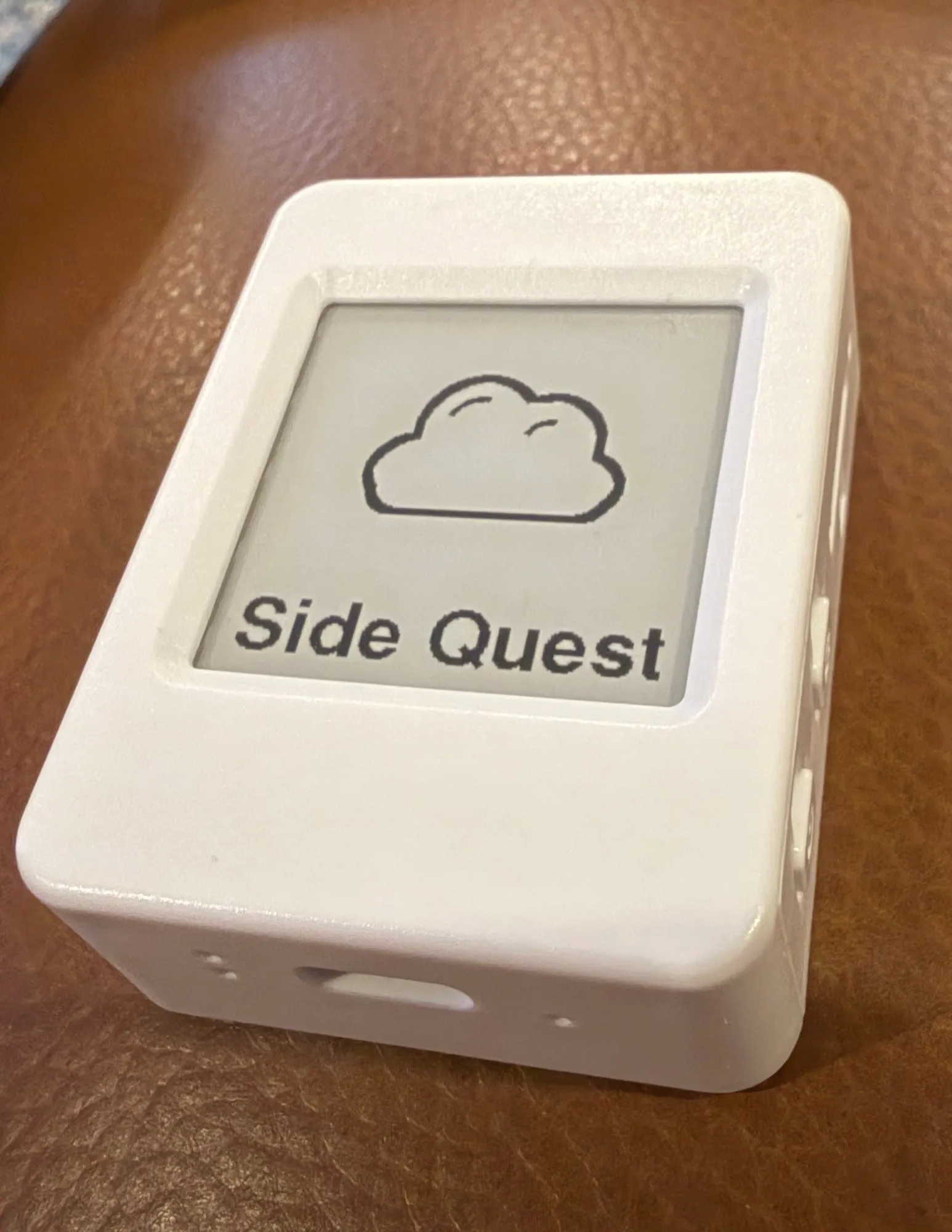 A white pocket device with an e-ink screen showing a cloud logo and the words Side Quest